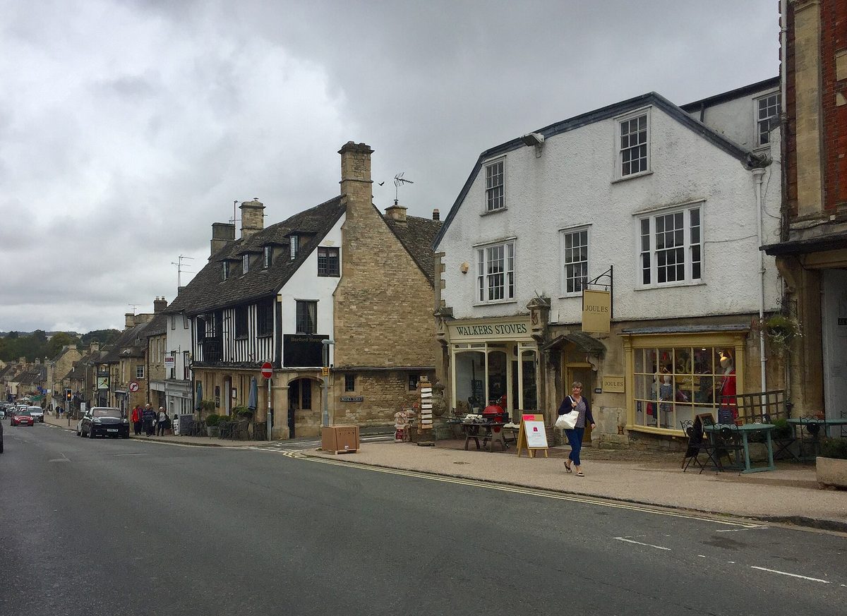 A sunny Cotswold pub garden with wooden tables and rolling green countryside behind