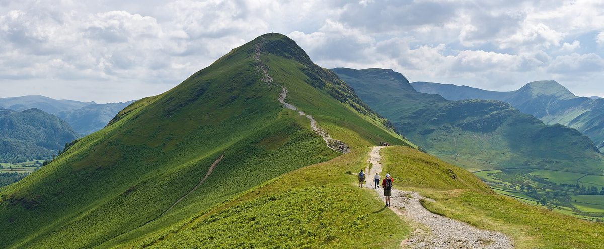A walker on the rocky summit ridge of Catbells above Derwentwater near Keswick, fells stretching to the horizon
