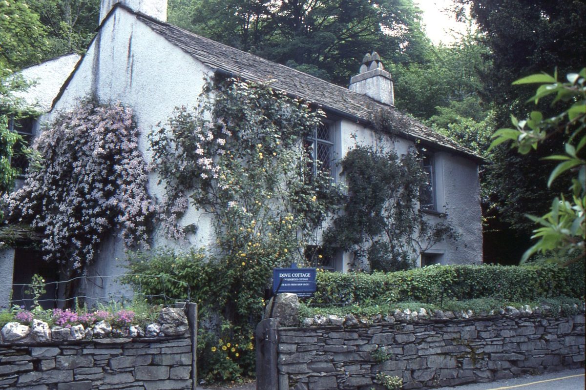 Dove Cottage in Grasmere with its whitewashed walls and small garden under a grey, drizzly Lake District sky, a classic rainy day visit