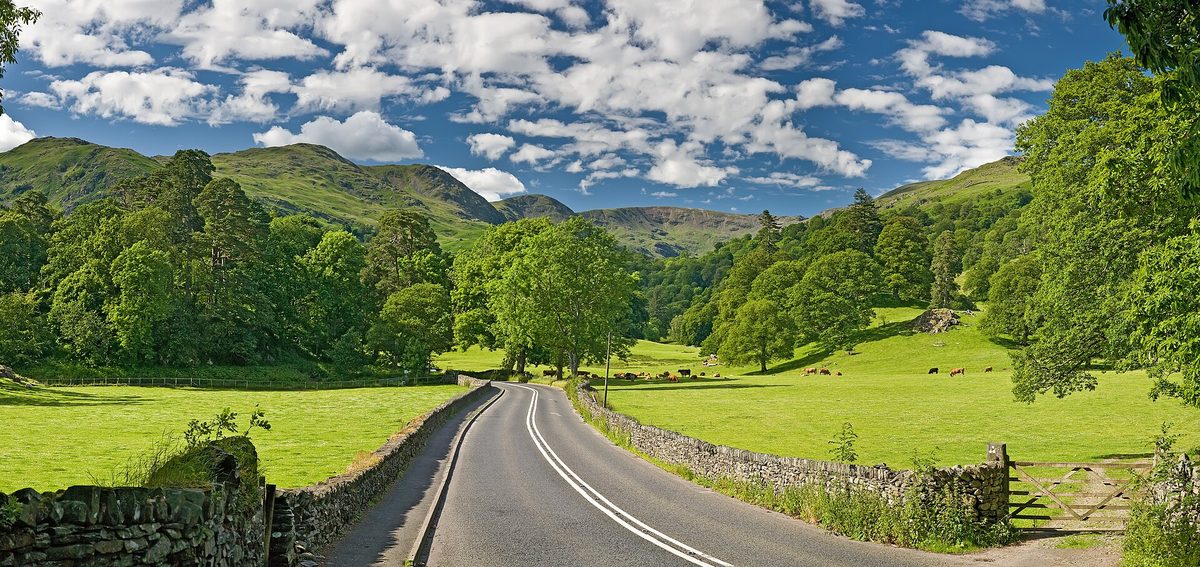A Lake District road curving past green hills and stone walls