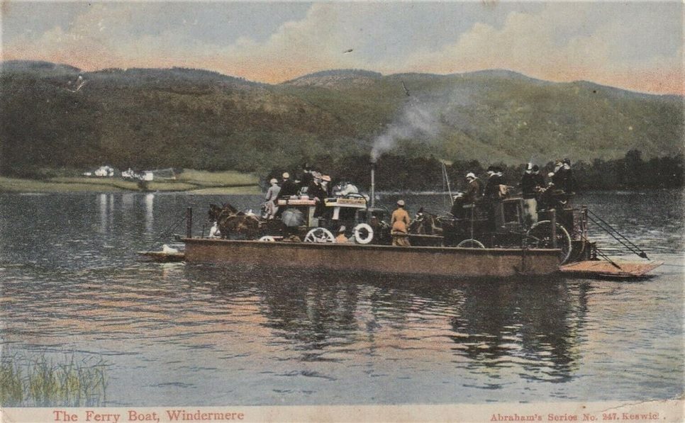 The small Windermere car-and-foot ferry mid-crossing on a calm grey lake, carrying a few vehicles to the western shore